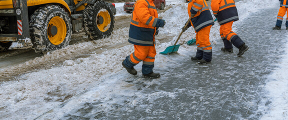 Three men in orange coats are shoveling snow from the road