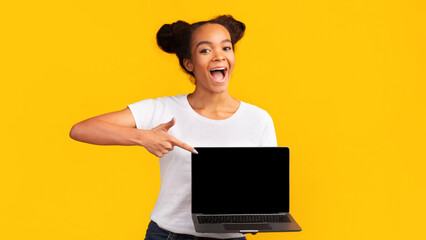 Awesome Application Or Website. Excited black girl showing blank laptop screen for advertising, mockup, empty space