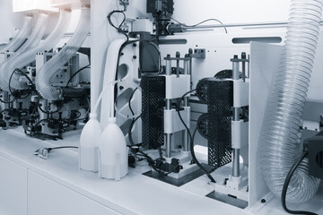 Poster - A machine with a white background and a white and clear plastic container on it. A machine is cutting a strip of wood. The machine is surrounded by other machines