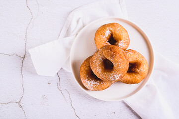 Close up of delicious donuts in powdered sugar on a plate on a white table top view