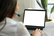 © Irina B - A woman using a laptop with a blank screen while sitting in a modern workspace, holding a pen and working on a task. mockup.