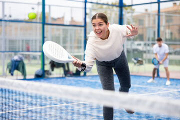 Wall Mural - Emotional young female paddle tennis player preparing to perform forehand to return ball on outdoor court on sunny autumn day..