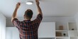 © gunzexx png and bg - A man is seen adjusting or fixing a ceiling light in a modern home, concentrating on home improvement and maintenance tasks, showcasing responsible household work in contemporary living spaces.