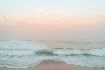 Wall Mural - A gentle wave crashes onto a sandy beach, with a soft pink sky above.