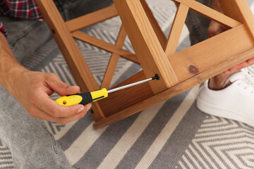 Poster - Man repairing wooden stool with screwdriver indoors, closeup