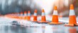 © nattapon98 - Traffic cones lining a misty road, creating a vibrant orange barrier, signaling construction or maintenance work ahead in a blurred urban environment.