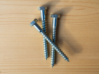 Galvanized hex steel lag bolts. Lag bolts and wood screws. Structural elements of wooden buildings and construction. A pile of screws on a wooden background 