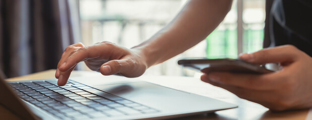 Close up of hands typing on laptop computer keyboard and working on internet.