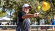 © Galib - An older man with a beard is playing tennis. He is holding a yellow racket and a ball is in the air.