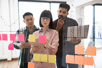 Wall Mural - Team of young professionals brainstorming and collaborating using sticky notes on glass wall in modern office. Discussion focused on project planning, organization, and innovation.