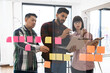 © sofiko14 - Colleagues collaborating on project brainstorming ideas using sticky notes on glass wall. Teamwork, communication, and creativity are emphasized. Modern office setting.