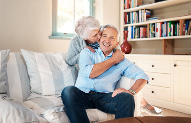 Canvas Print - Kiss, portrait and elderly couple on sofa for connection, bonding and relaxing together at home. Smile, love and senior man and woman hugging for resting in living room at house in Switzerland.