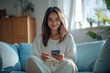 © Niks Ads - young beautiful woman sitting on sofa holding smartphone and smiling