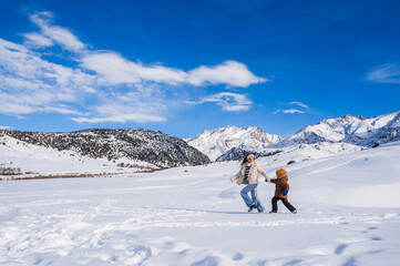 Wall Mural - Mom and son running in the snow on the background of a mountain landscape in winter.