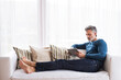 © Halfpoint - Man at home, watching tv show on tablet, sitting on sofa with feet up, feeling cozy.