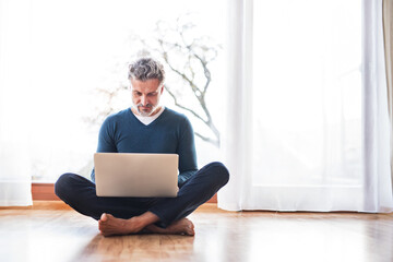 Wall Mural - Homeoffice for handsome man. Man sitting on floor and working on laptop. Telecommuting.