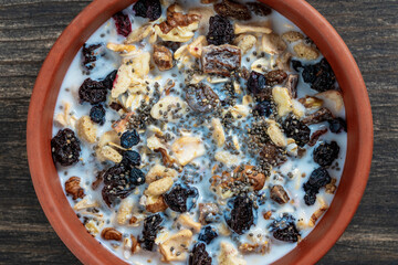 Whole grain oat muesli with dried fruits, nuts, raisins, berries and almond milk in clay bowl on wooden table, top view, closeup. Background of organic muesli for breakfast