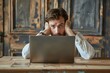 © Michael - Stressed young man holding his head feeling frustrated working on laptop computer at wooden desk