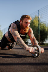 Bearded sportsman in weighted vest training with ab roller in park