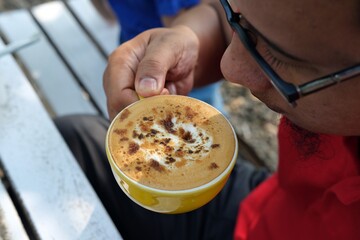 A close-up shot of a hand holding a cup of crème brûlée coffee, topped with caramelized sugar in a vibrant yellow cup. Perfect for coffee advertisements, cafe menus, or social media campaigns.