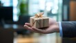 © sarana - Hand Offering a Gift Box in a Business Setting: A professional hand presenting a small, elegantly wrapped gift box in an office environment.