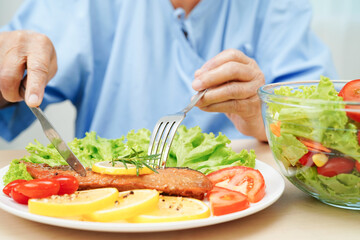 Wall Mural - Asian elderly woman patient eating salmon stake and vegetable salad for healthy food in hospital.