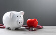 © SKT Studio - white piggy bank, a stethoscope, and a red heart are placed on a table. The image symbolizes the connection between financial planning, health care, and well-being.
