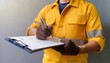 © TransPicHub - A construction worker in a yellow jumpsuit signs a document on a clipboard.