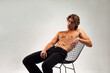 © Alex Vog - Handsome young man muscular fashion model with muscle abs press sitting on chair, positive looking away. Studio shot of sporty strong muscle guy with sexy bare torso on white. Copy ad text space