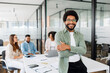 © Vadim Pastuh - Young man stands with arms crossed in modern office space, showcasing relaxed yet professional work environment, behind him diverse team of colleagues engages in a productive and collaborative meeting