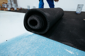 Construction worker installing roofing felt on roof with bitumen rolls