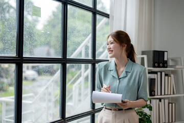 Wall Mural - A woman is standing in front of a window with a piece of paper in her hand