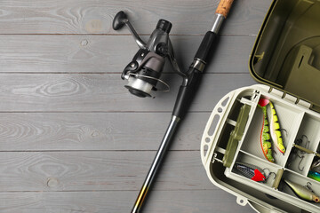 Sticker - Different fishing tackles in box and rod with spinning reel on grey wooden table, top view. Space for text