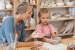 © ulza - mother and child daughter makes a cup of clay crafts pottery school. A professional potter teaching and coaching kid making a pottery in the workshop.