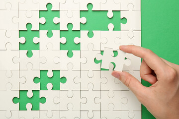 Wall Mural - Woman solving white puzzle on green background, closeup