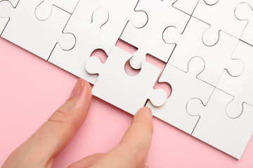 Wall Mural - Woman solving white puzzle on pink background, closeup