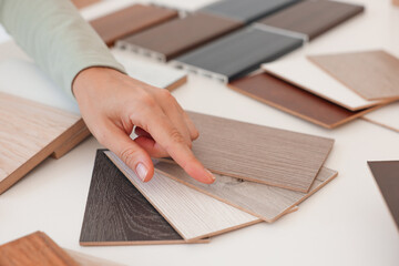 Wall Mural - Woman choosing wooden flooring among different samples at table, closeup