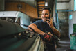© Miljan Živković - Car mechanic hold drill in auto repair shop talk on a mobile phone