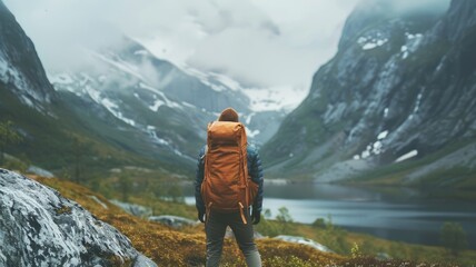 Backpacker with orange and yellow backpack overlooking a mountain lake in autumn. Attractive traveler or explorer standing and looking at mountain. Adventure and travel concept for design. AIG53.