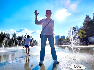 A person enjoys the refreshing splashes from fountains in a lively city park on a bright, sunny afternoon