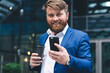 © BullRun - Half length portrait of cheerful male entrepreneur with takeaway cup with tasty caffeine beverage using cellphone application for checking financial news on website, concept of business people