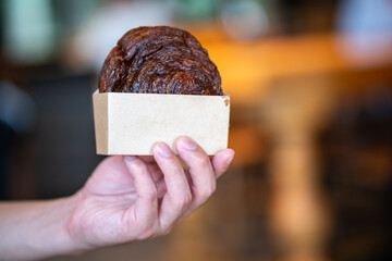 Close up hand of person holding appetizing baked sweet cinnamon roll in paper box.
