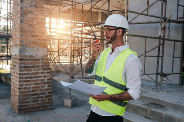 Construction industry workers talking on the radio communicating with workers planning using blueprint design, engineer architects, Male caucasian development working in building site structure.