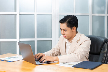 Asian businessman working in his office reviewing work, accessing planning strategy, creative thinking and innovation ideas, sitting at desk typing on laptop computer keyboard, professional worker.