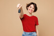 © ViDi Studio - Young smiling happy woman she wear red t-shirt casual clothes hold in hand car key fob keyless system stretch hand to camera isolated on plain pastel light beige background studio. Lifestyle concept.