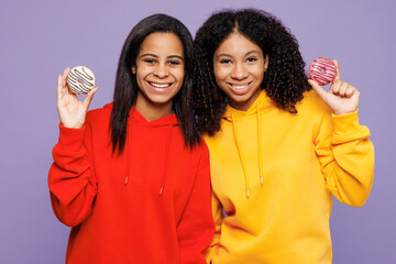 Wall Mural - Two young fun little kid teen girls women they wear red yellow hoodie casual clothes hold in hand sweet yummy donuts looking camera isolated on plain pastel light purple background. Lifestyle concept