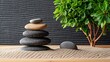 © Anchalee - Balanced stones stacked on sand next to a green plant, creating a serene and tranquil zen garden scene.