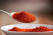 © Nut Cdev - Close-up view of spicy red chili pepper powder being poured from a spoon with a blurred background.