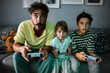 © Marko Geber - Father playing video games with his son and daughter at night in the living room