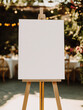 © NILSEN Studio - A blank canvas on an easel stands outdoors, framed by festive string lights and greenery, offering a perfect space for creative expression in a celebratory environment. Mockup.